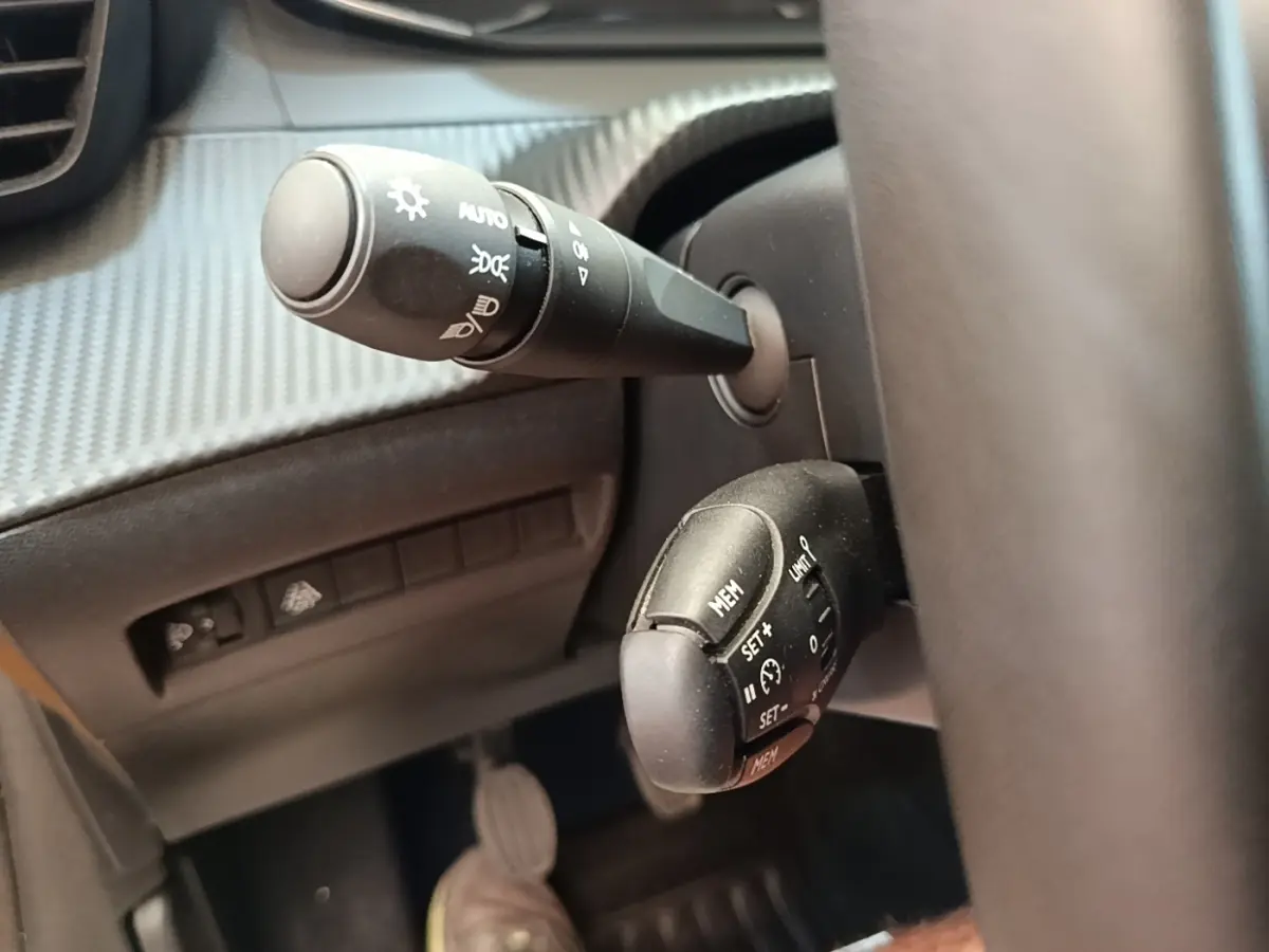 Gros plan sur la commande de régulateur de vitesse et les commandes d’éclairage du Peugeot 208 PureTech jaune, côté conducteur.