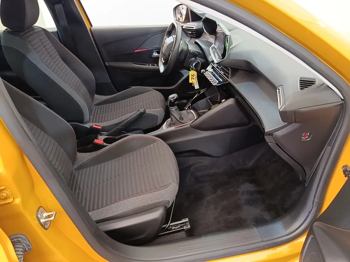 Intérieur avant droit d'une Peugeot 208 jaune 2023, volant cuir multifonctions et tableau de bord avec écran tactile.