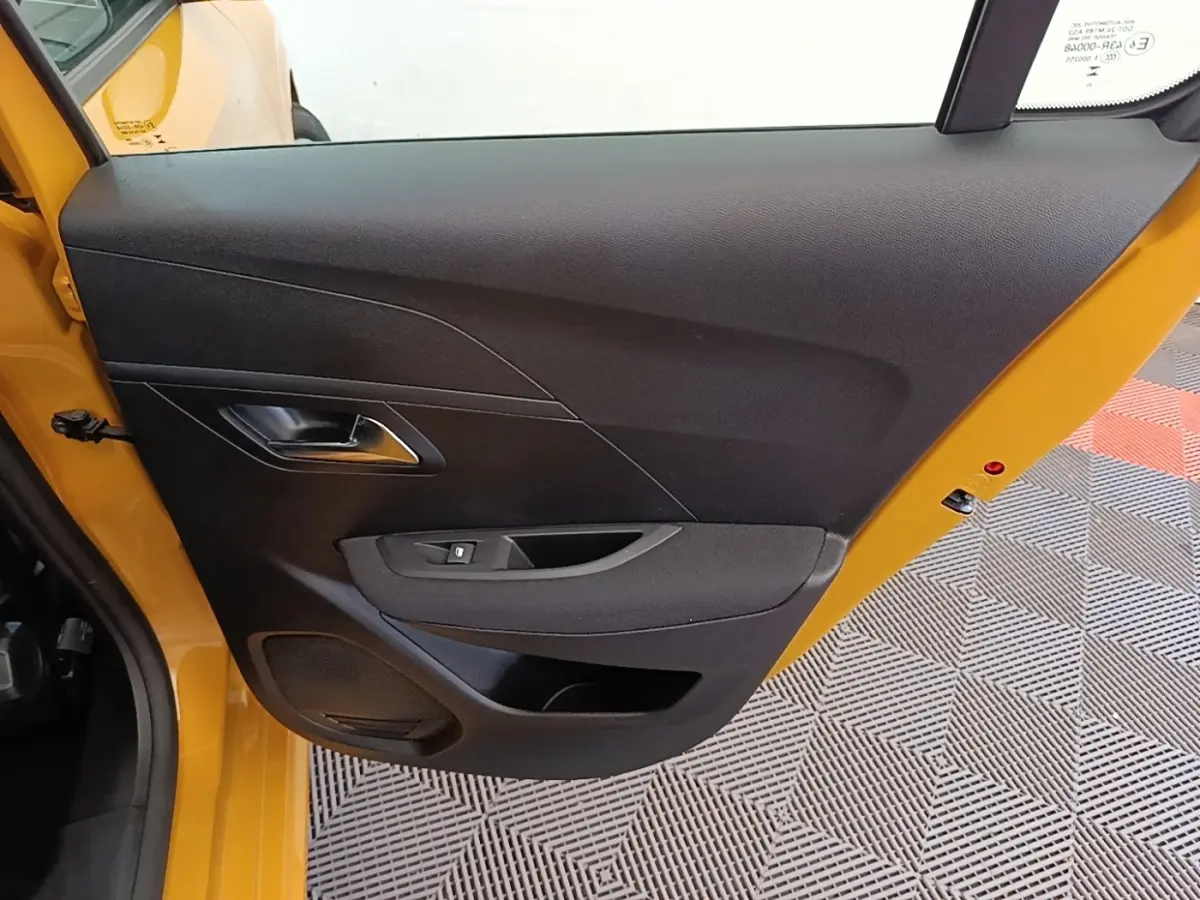 Vue rapprochée de la porte avant gauche noire d’une Peugeot 208 jaune 2023, avec poignée et commande de vitre.