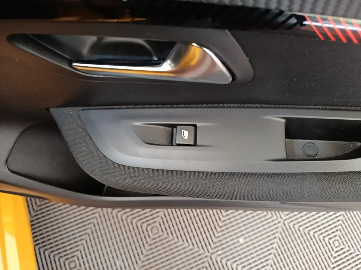 Détail de la porte côté conducteur d’une Peugeot 208 jaune 2023, avec poignée argentée et bouton de lève-vitre.