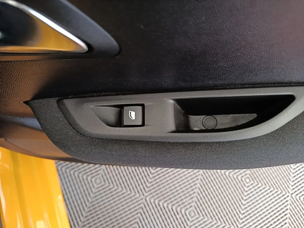 Détail de la commande de lève-vitre électrique sur la porte intérieure côté conducteur d'une Peugeot 208 jaune.