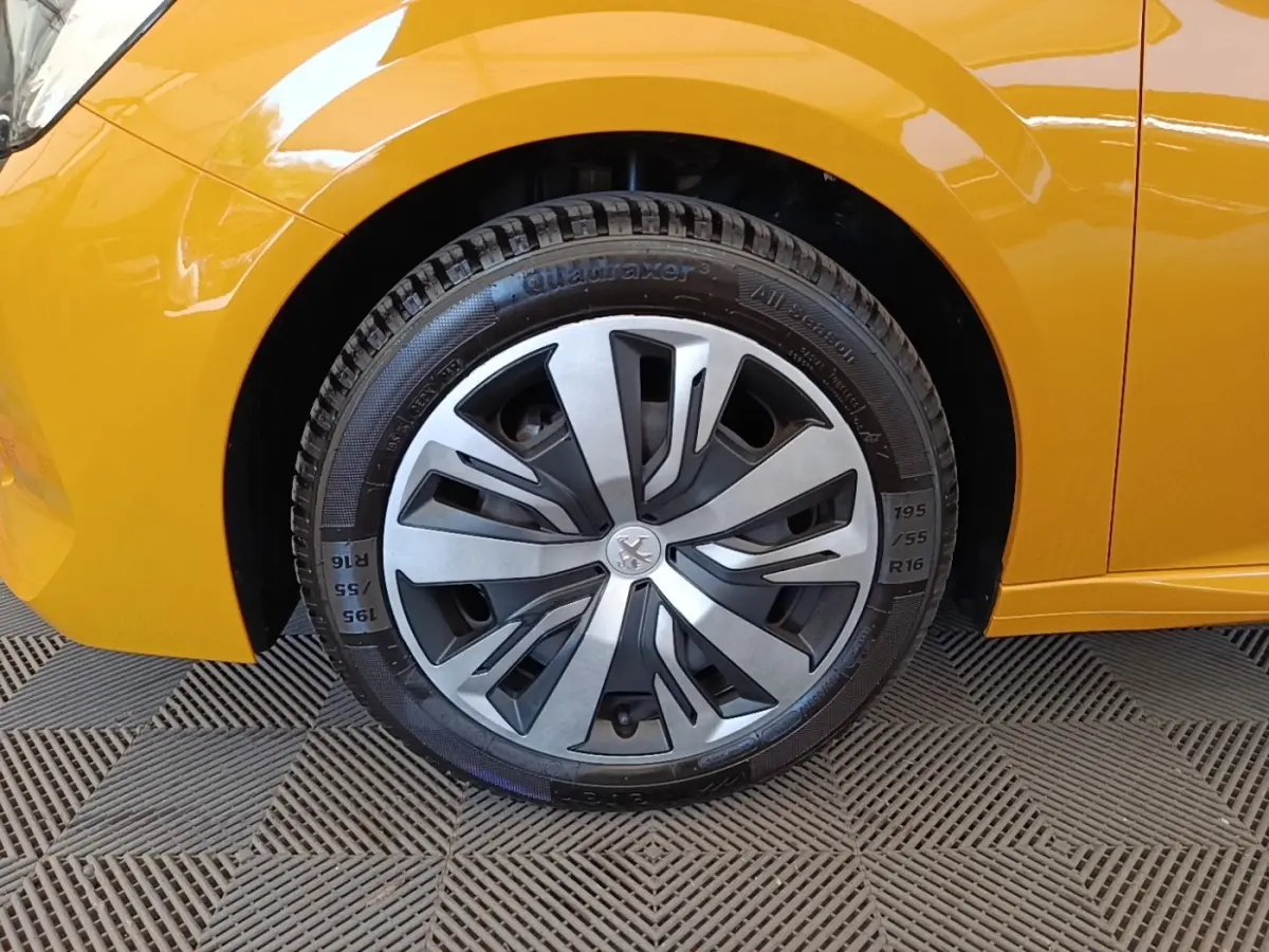 Gros plan sur la roue avant gauche d’une Peugeot 208 jaune 2023 avec jante en alliage au design moderne.