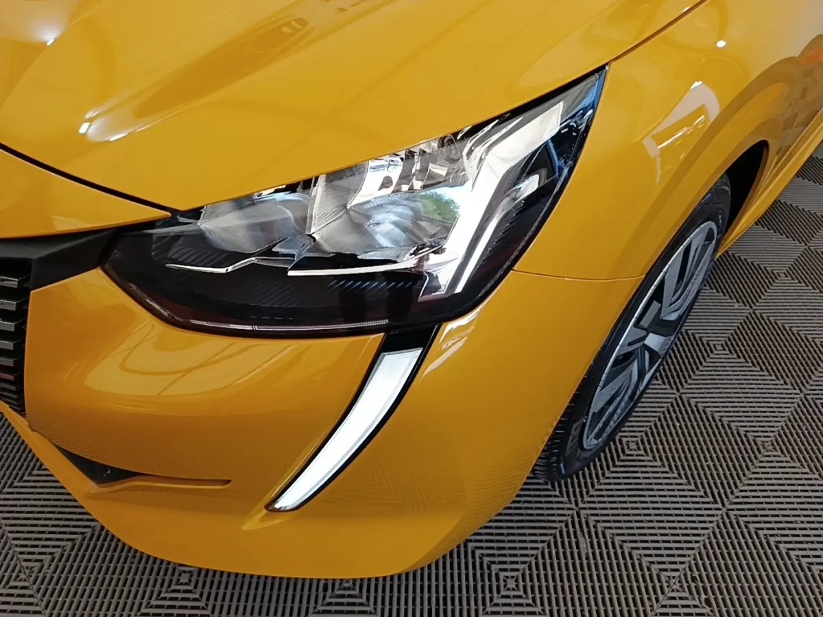 Gros plan sur le phare avant gauche et la roue d’une Peugeot 208 jaune PureTech 75 S&S Active Pack 2023.
