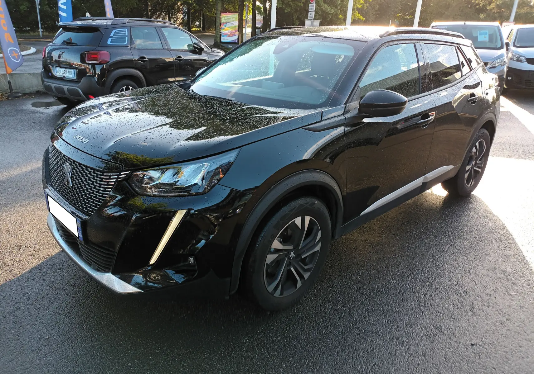 PEUGEOT 2008 noir vue 3/4 avant droit avec feux LED et jantes alliage bicolores sur parking humide.