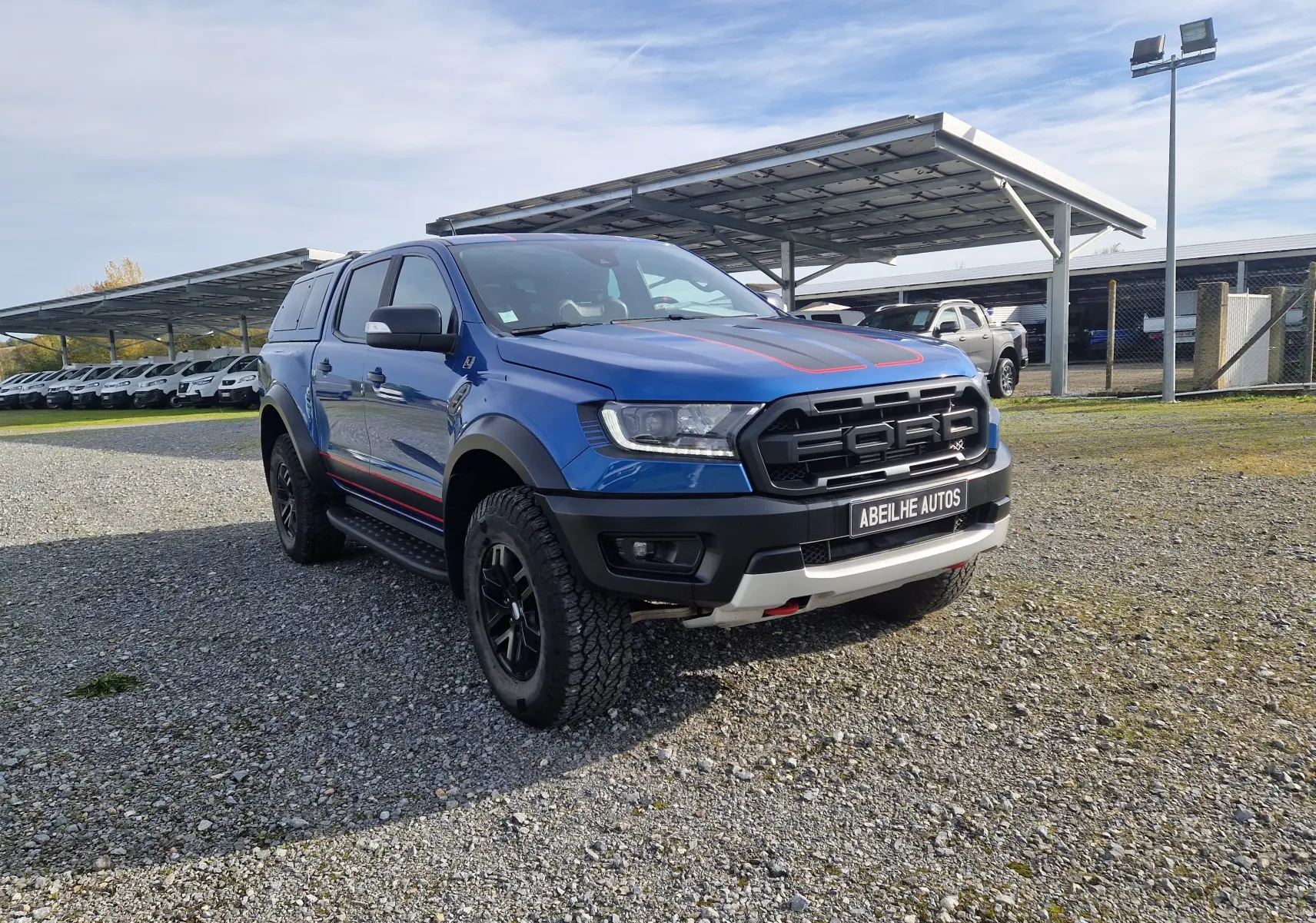 Ford Ranger Double Cabine Raptor bleu Ford Performance en 3/4 avant droit avec bandes rouges et hard top noir.