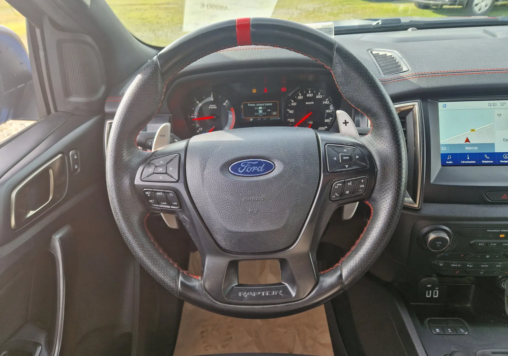 Vue intérieure centrée sur le volant en cuir noir avec surpiqûres rouges du Ford Ranger Raptor 2022, tableau de bord et écran tactile visibles.
