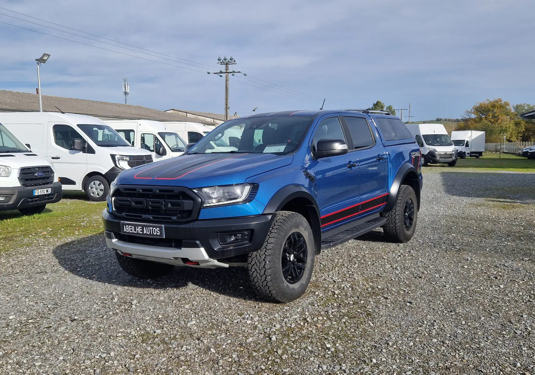 Ford Ranger Raptor bleu Ford Performance vu en 3/4 avant droit, avec hard top et marquages rouges sur capot et flancs.