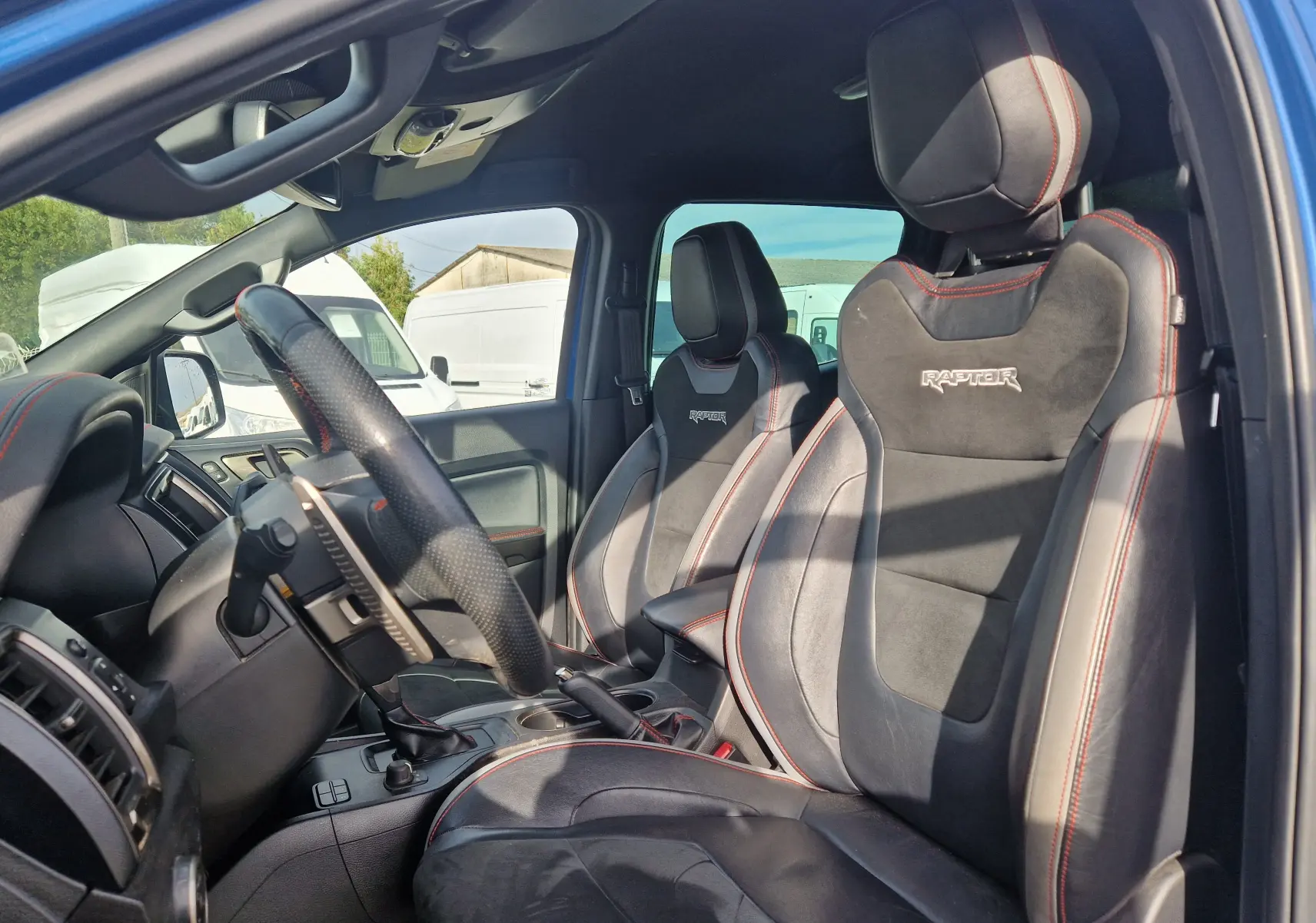 Vue intérieure côté conducteur du Ford Ranger Raptor 2022, sièges en cuir noir avec surpiqûres rouges et logo Raptor brodé.