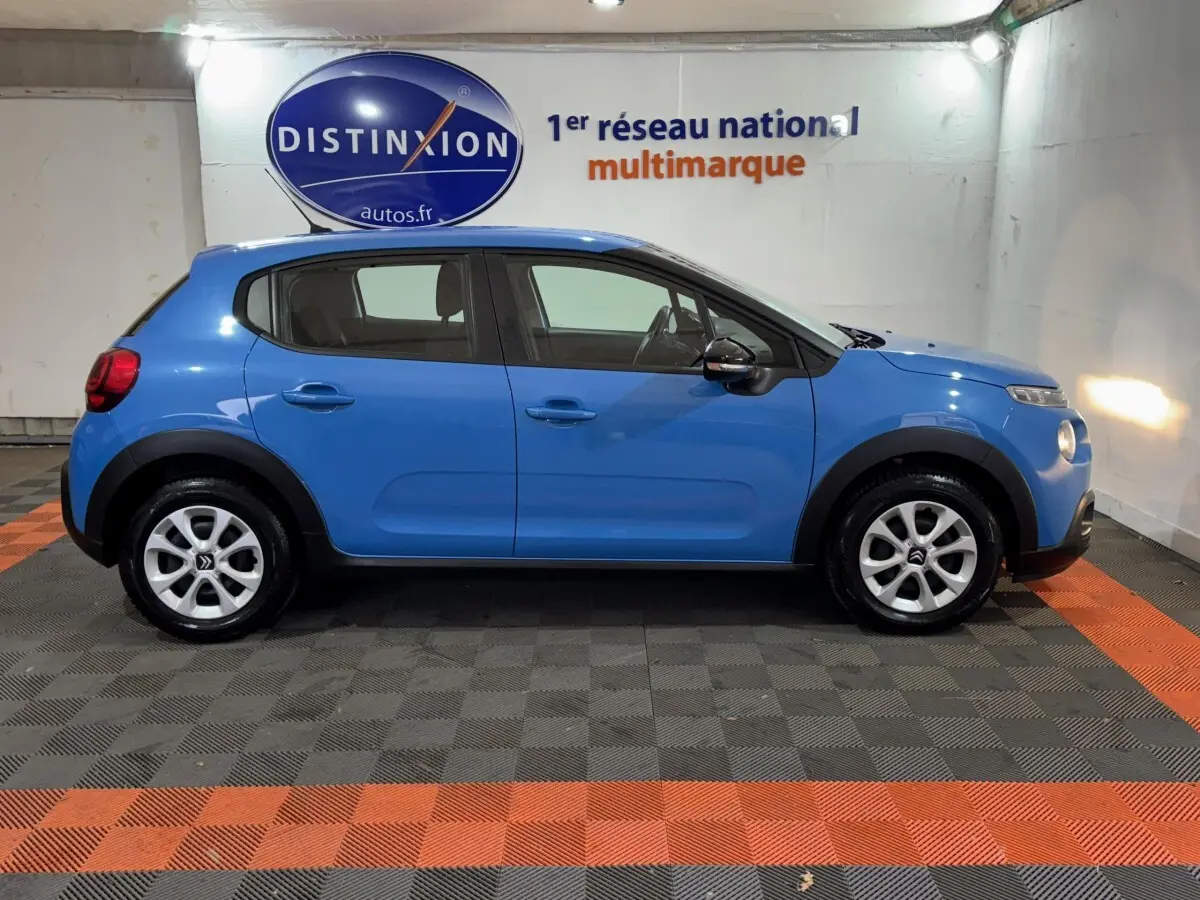 Profil côté gauche d'une Citroën C3 bleu 2018 dans un showroom avec sol à damier noir et orange.