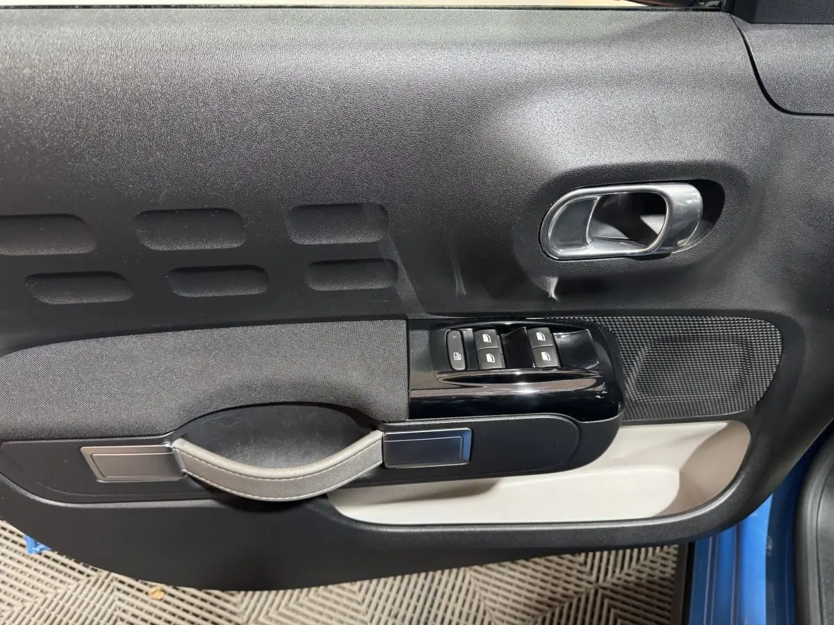 Vue rapprochée de la porte avant gauche bleu Citroën C3, avec poignée argentée et commandes de vitres noires.