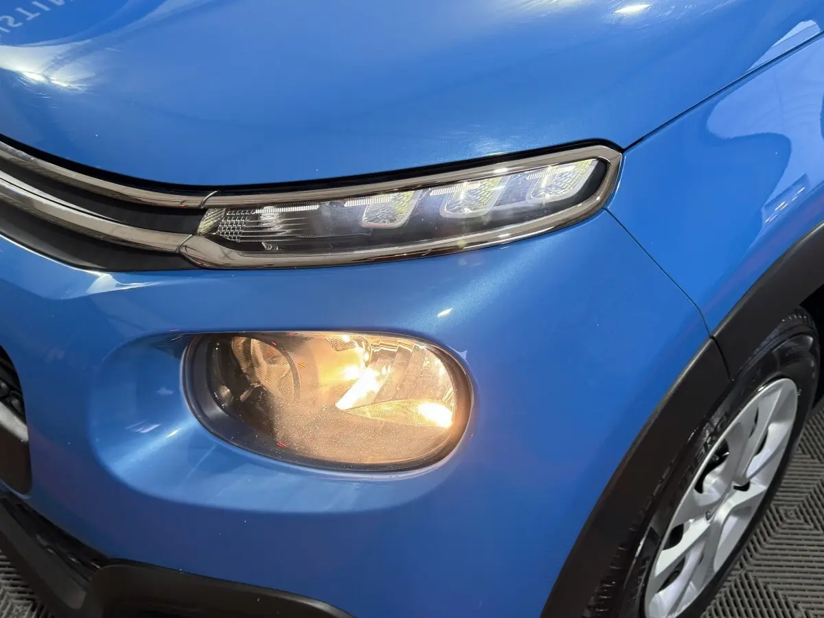 Gros plan sur le phare antibrouillard avant droit allumé d'une Citroën C3 bleu vif, avec partie du capot et roue visible.