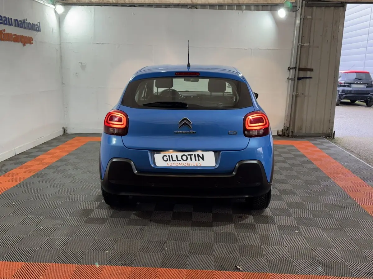 Vue arrière d'une Citroën C3 bleu vif avec feux arrière allumés dans un garage éclairé.