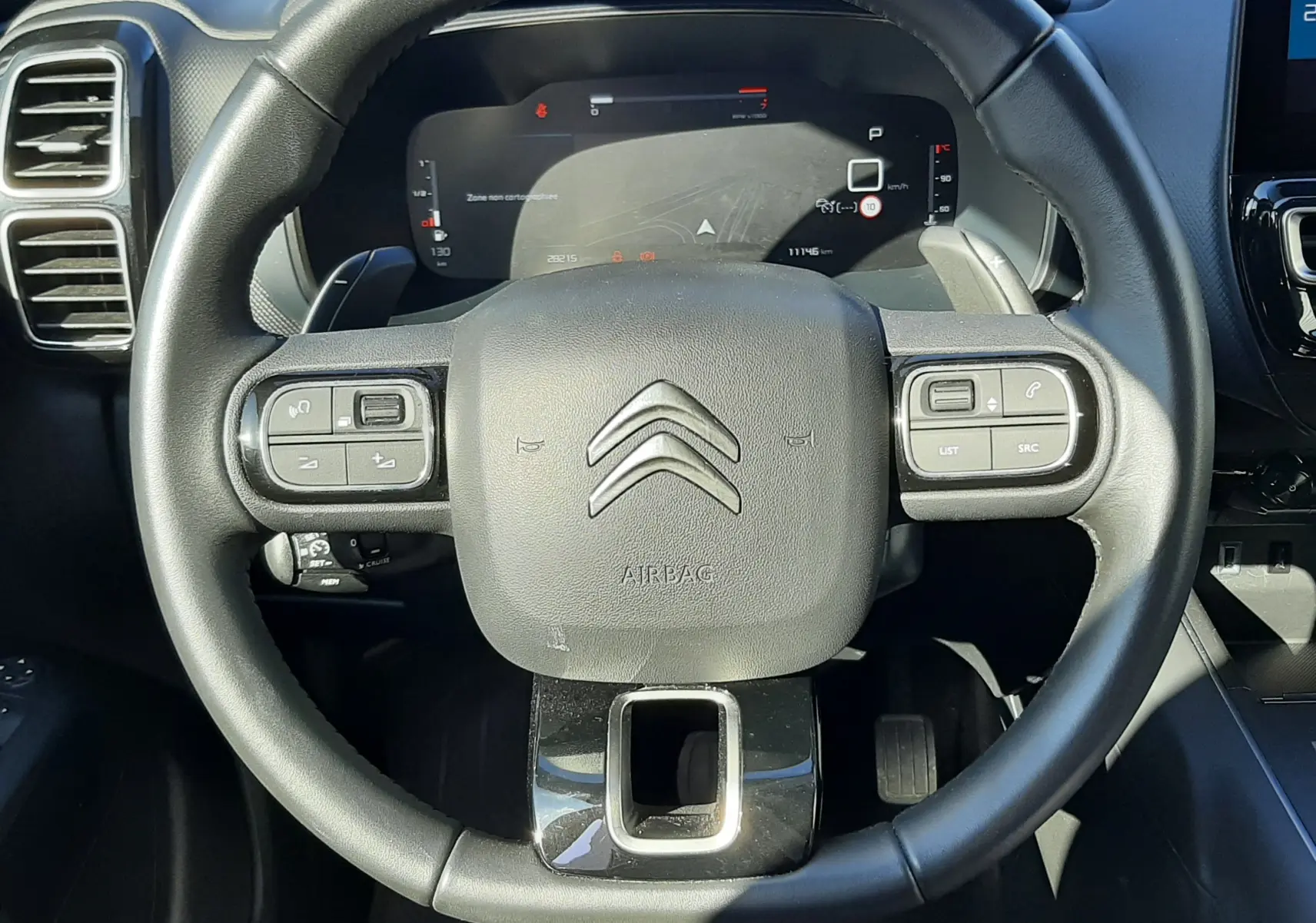 Vue rapprochée du volant noir du Citroën C5 Aircross 2024, avec commandes intégrées et tableau de bord numérique visible.