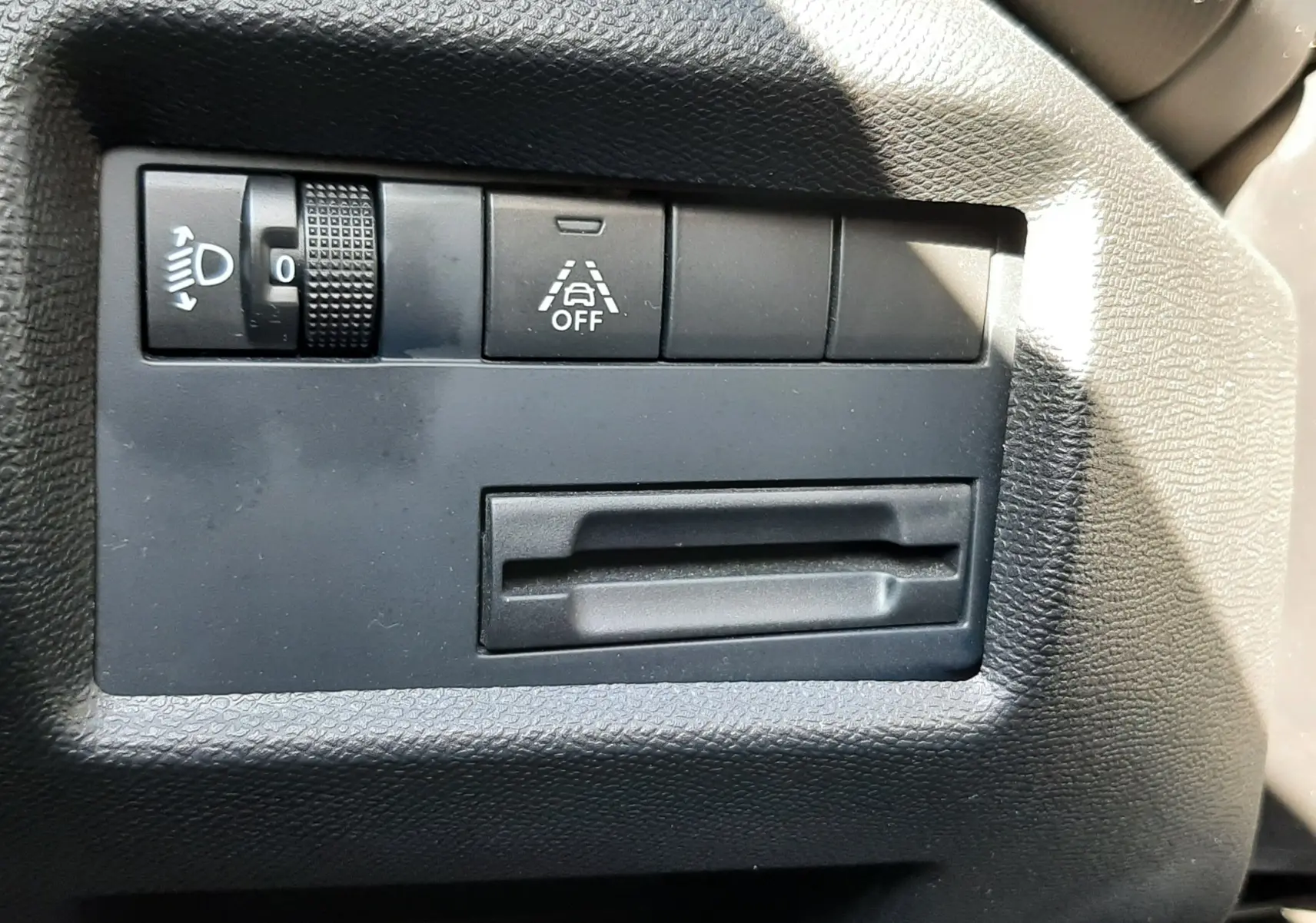 Détail du tableau de bord côté gauche du Citroën C5 Aircross noir, avec commande de réglage des phares et bouton d'assistance à la conduite.