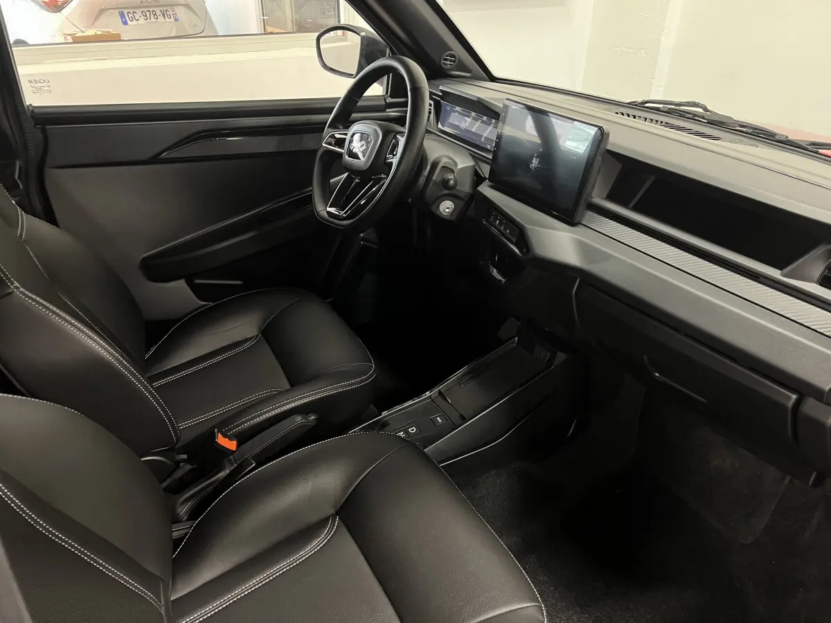 Vue intérieure avant droite de la LIGIER JS50 BEV 8KWH ELITE 2025 avec sièges noirs et écran tactile central.