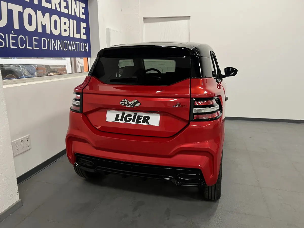Vue arrière d'une Ligier JS50 BEV 8KWH ELITE rouge avec toit noir et feux arrière LED dans un showroom.
