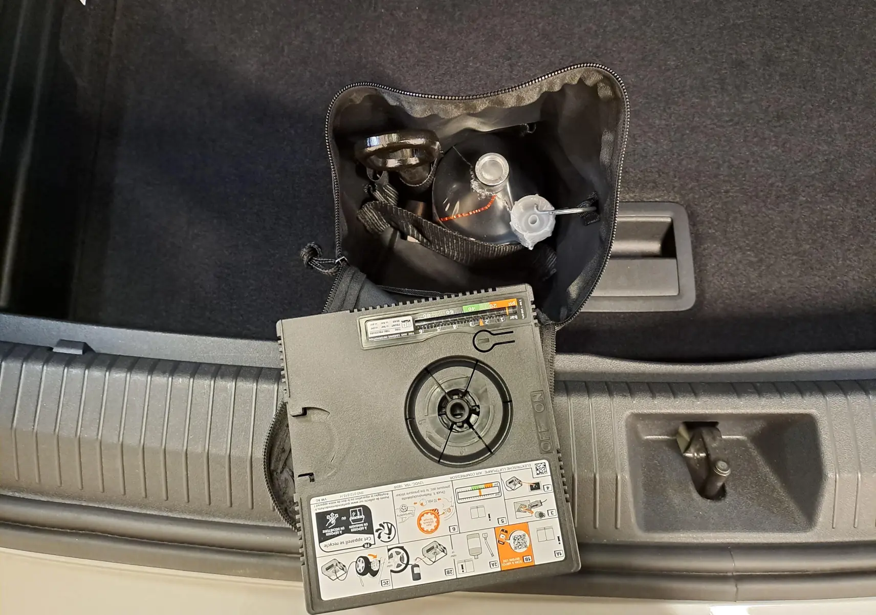 Vue plongeante sur le coffre d'un Volkswagen Tiguan argent Dolomite, montrant un kit de réparation pneu et compresseur.