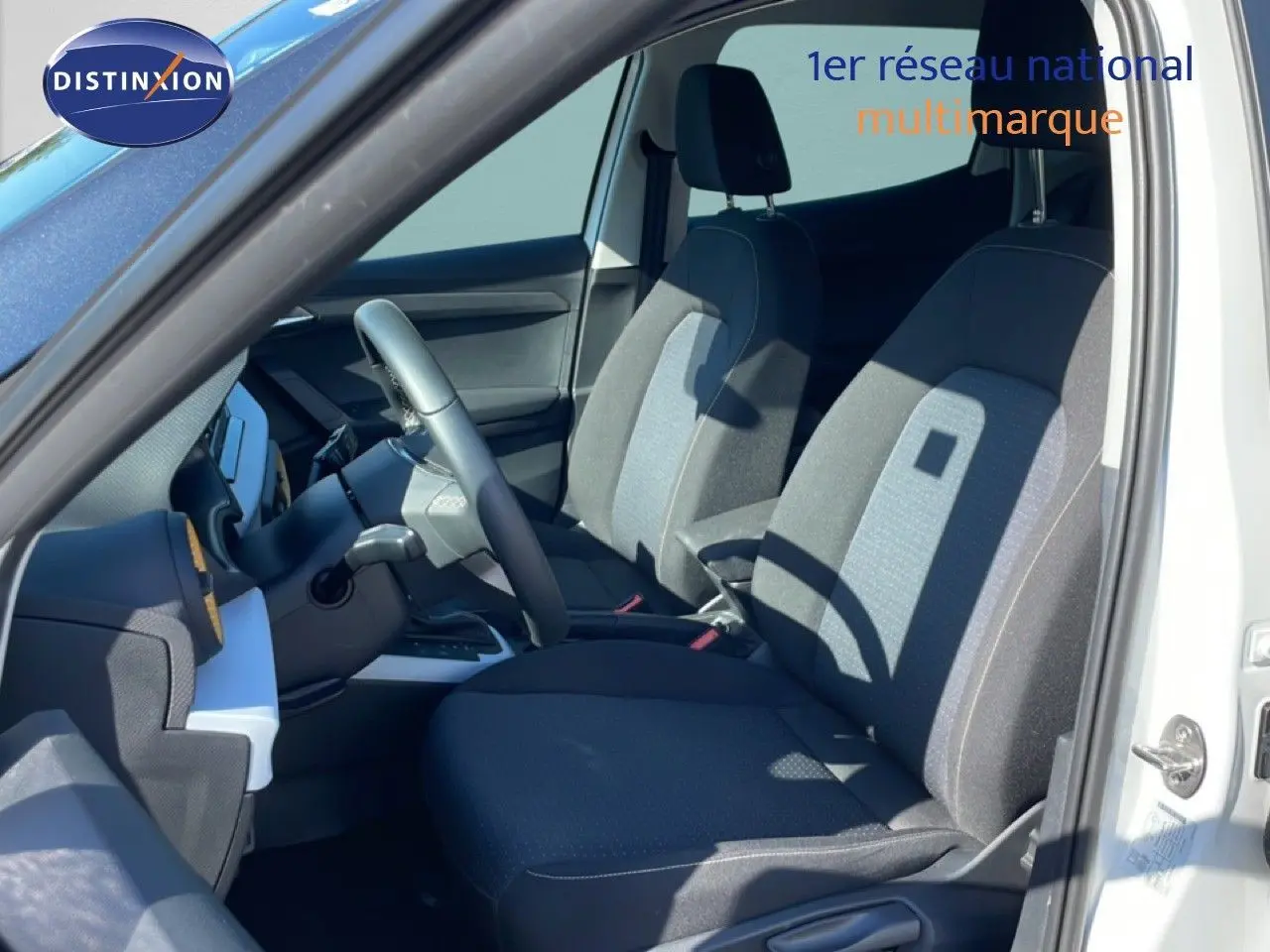 Vue intérieure côté conducteur du SEAT Arona blanc, montrant les sièges tissu noir et gris et le volant multifonction.