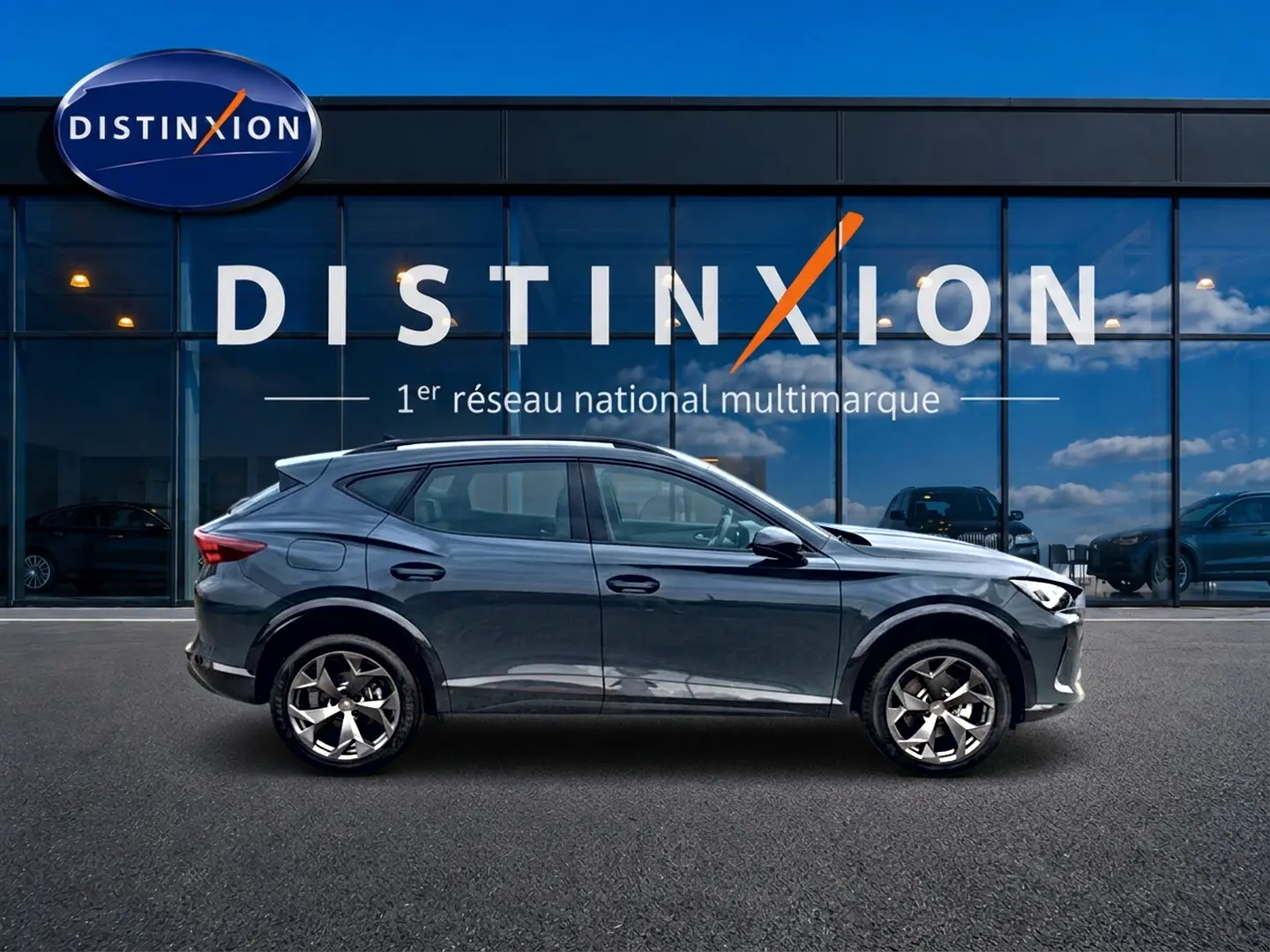 Vue latérale droite d'un CUPRA Formentor 1.5 etsi hybrid bleu fjord garé devant une vitrine avec logo Distinxion.