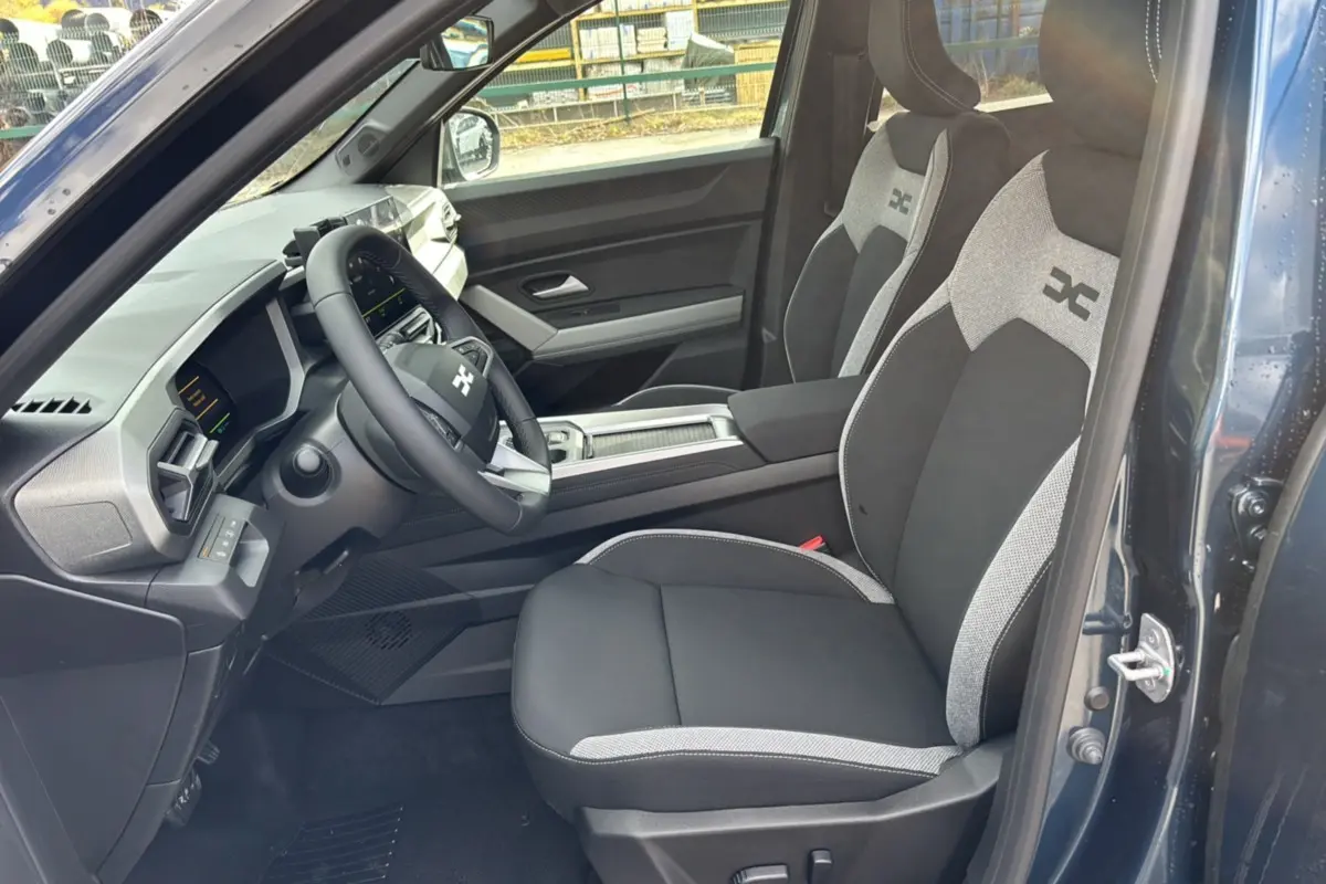 Vue intérieure côté conducteur du Dacia Bigster Hybrid 155 Journey Plus 2026 bleu indigo, sièges tissu noir et gris avec logo.