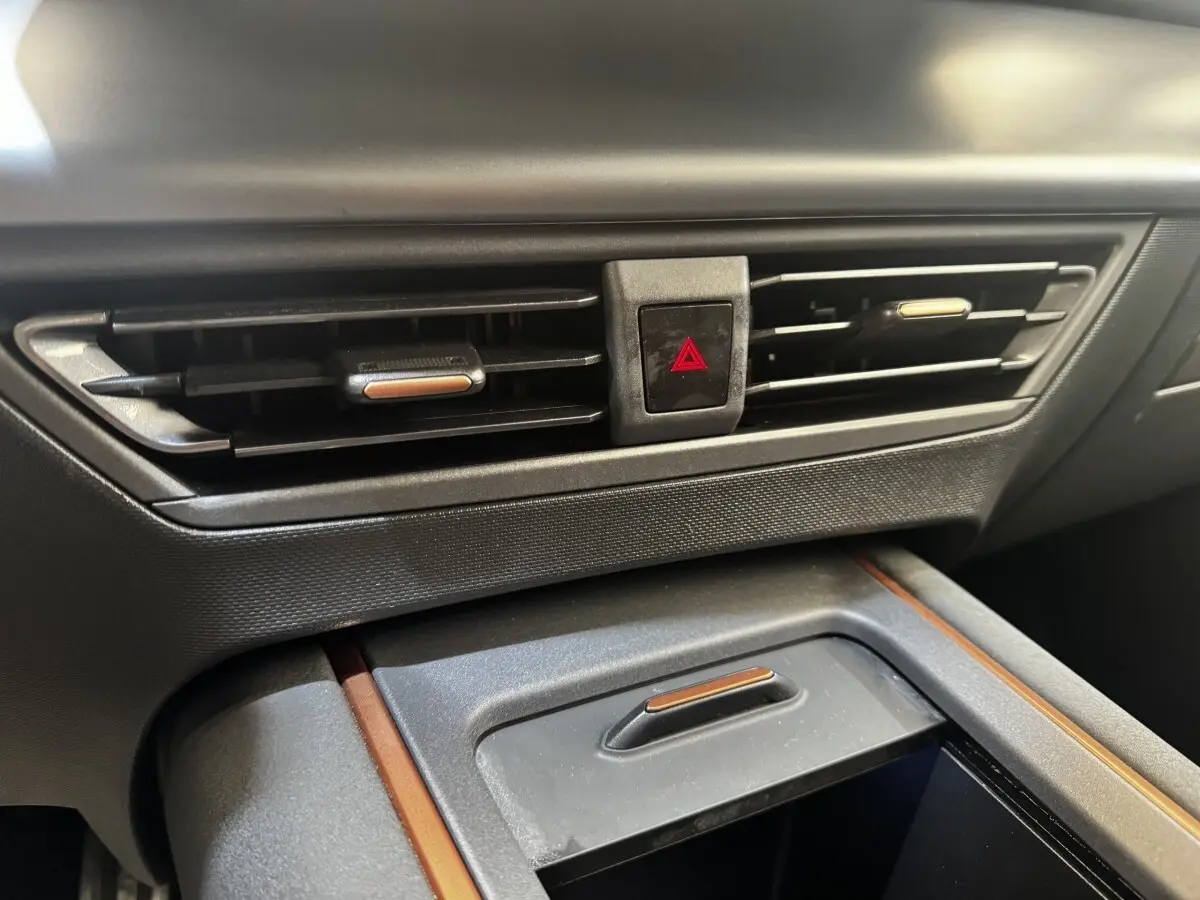 Gros plan sur la console centrale intérieure grise du CUPRA BORN 230ch, avec aérateurs et bouton de signalisation d'urgence rouge.