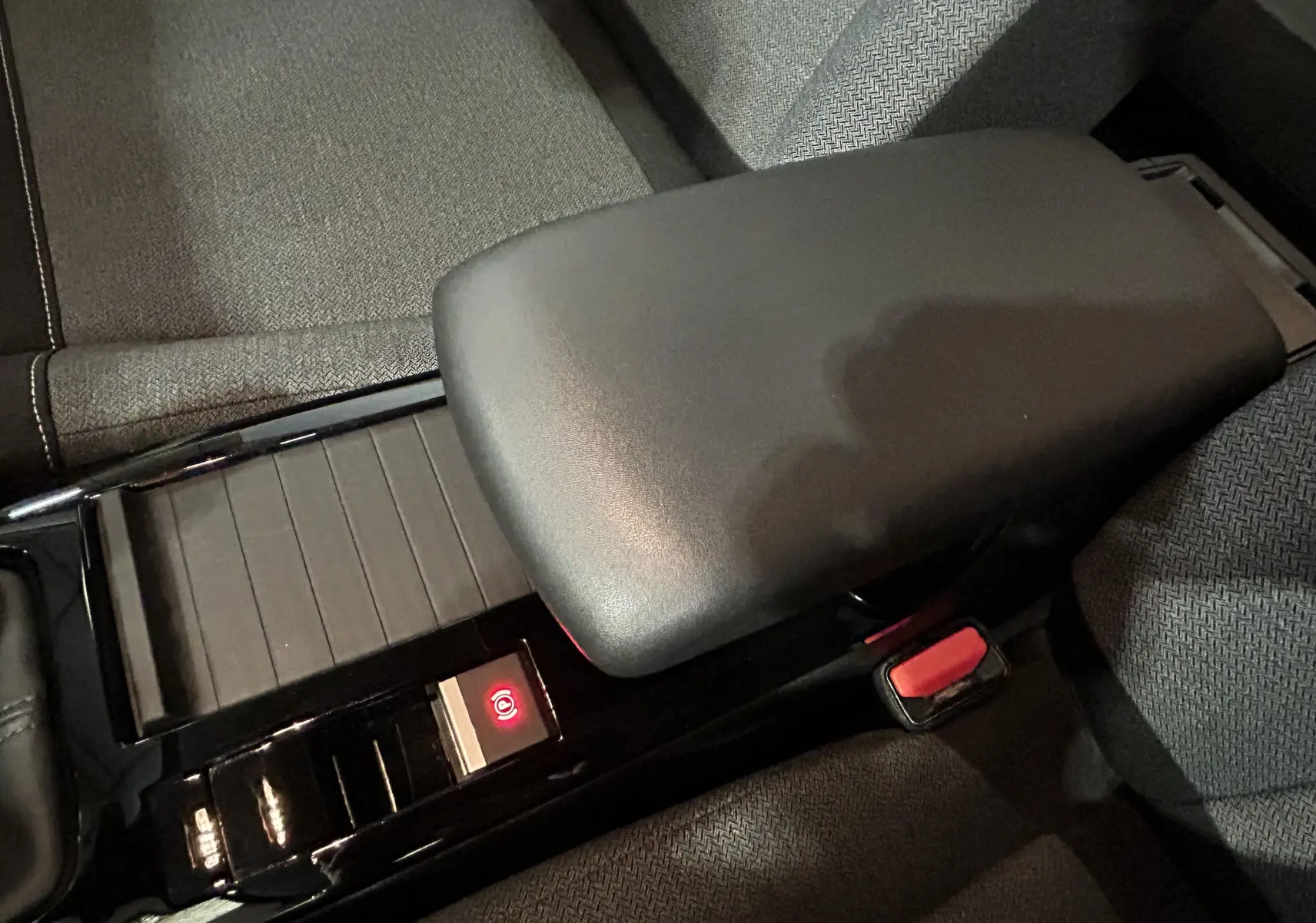 Gros plan sur l'accoudoir central noir et la console brillante avec frein à main électronique dans l'habitacle tissu gris d'une Citroën C4.