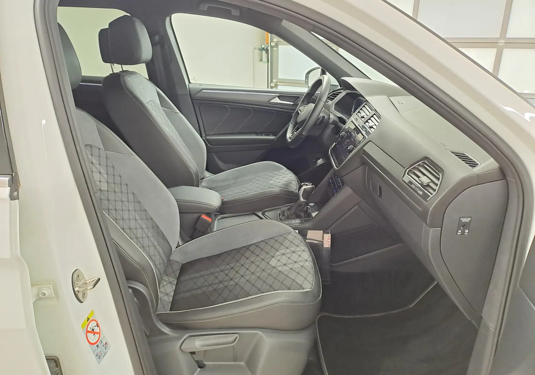 Vue intérieure côté conducteur du Volkswagen Tiguan Allspace blanc pur 2023, sièges en tissu noir à motifs géométriques.