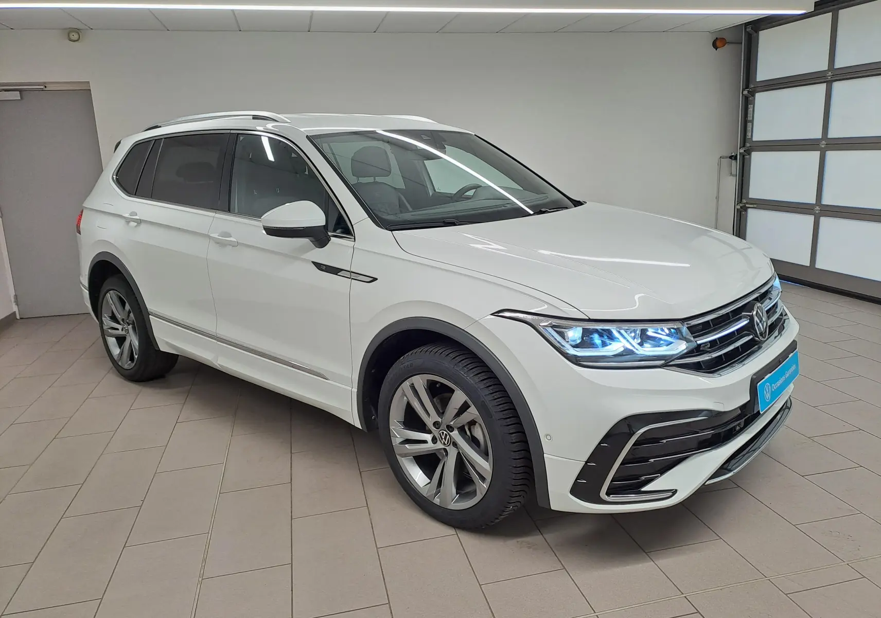 Vue 3/4 avant d'un Volkswagen Tiguan Allspace blanc pur 2023 en finition R-Line avec phares LED allumés.
