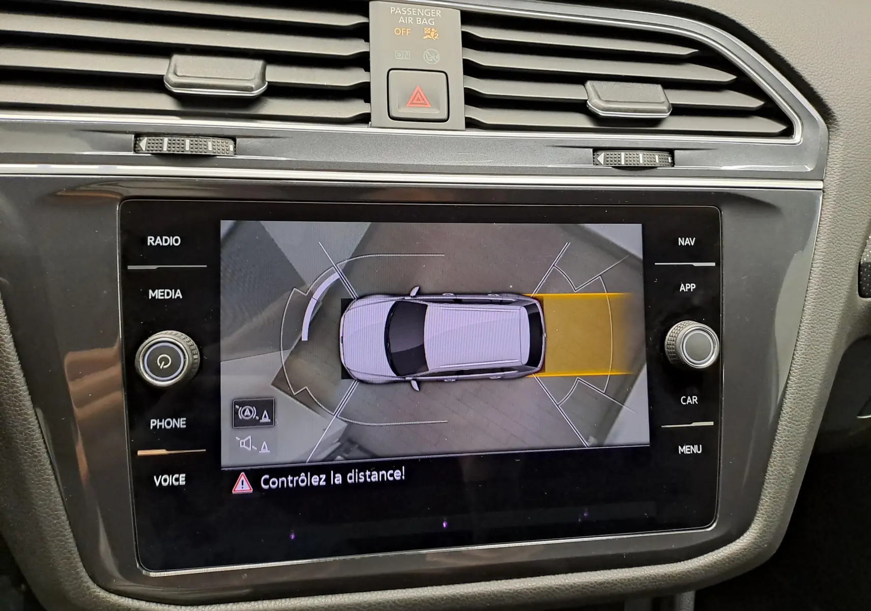 Vue de dessus de l'écran multimédia du Volkswagen Tiguan Allspace blanc, affichant l'aide au stationnement avec alerte de distance.