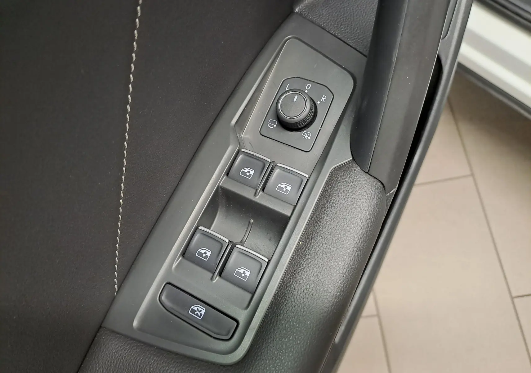 Gros plan sur les commandes de lève-vitres et réglage des rétroviseurs côté conducteur du Volkswagen Tiguan Allspace blanc 2023.