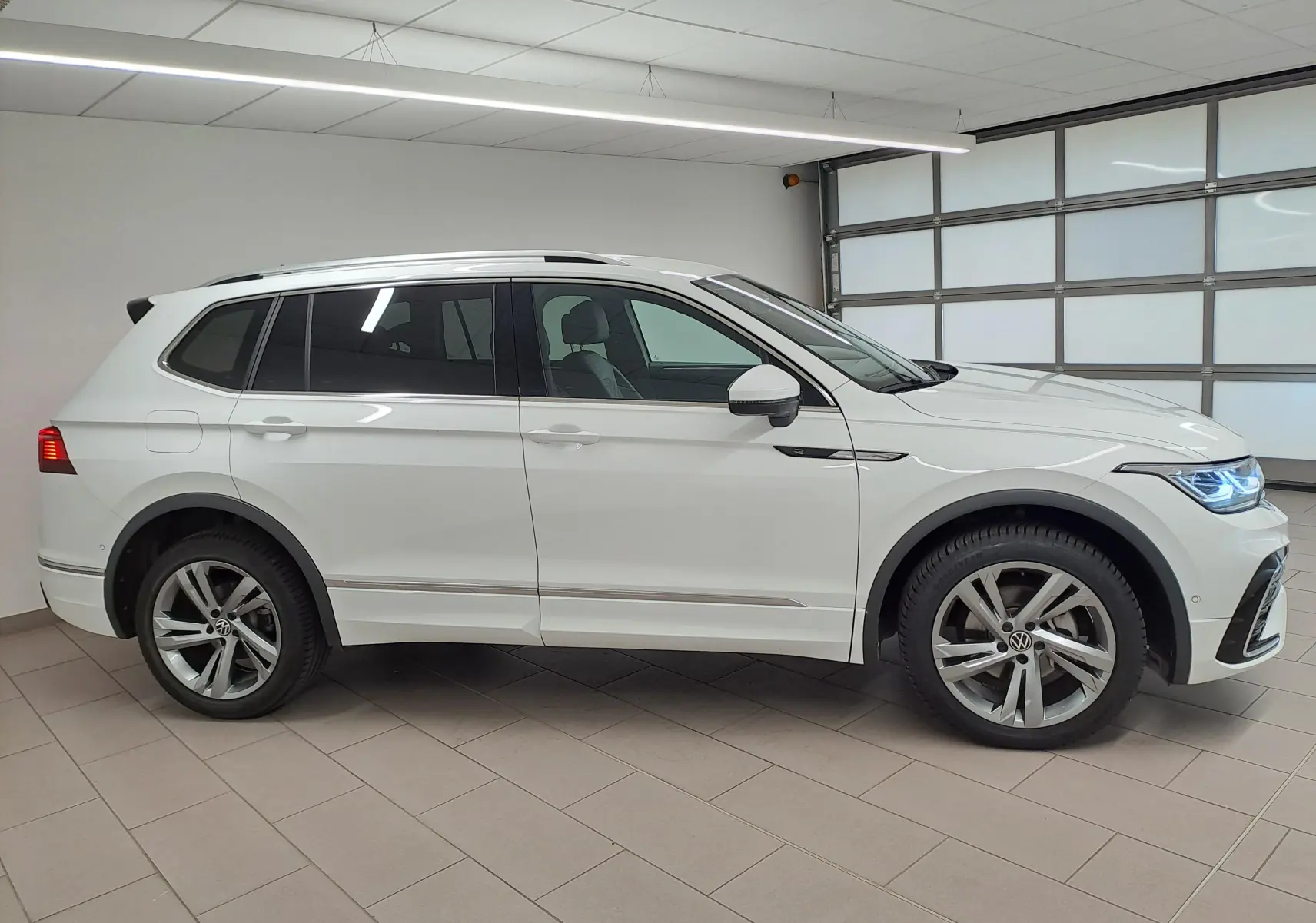 Vue de profil côté gauche du Volkswagen Tiguan Allspace blanc pur 2023 en finition R-Line avec jantes alliage distinctives.