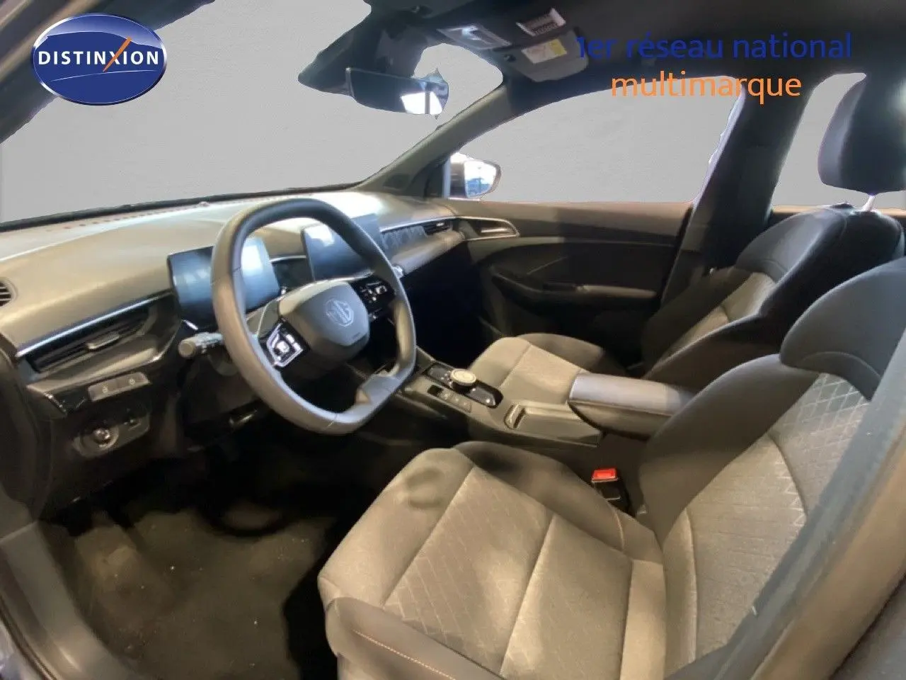 Intérieur de la MG3 1.5 Hybrid 2024 vu côté conducteur, sièges tissu gris noir et tableau de bord moderne.