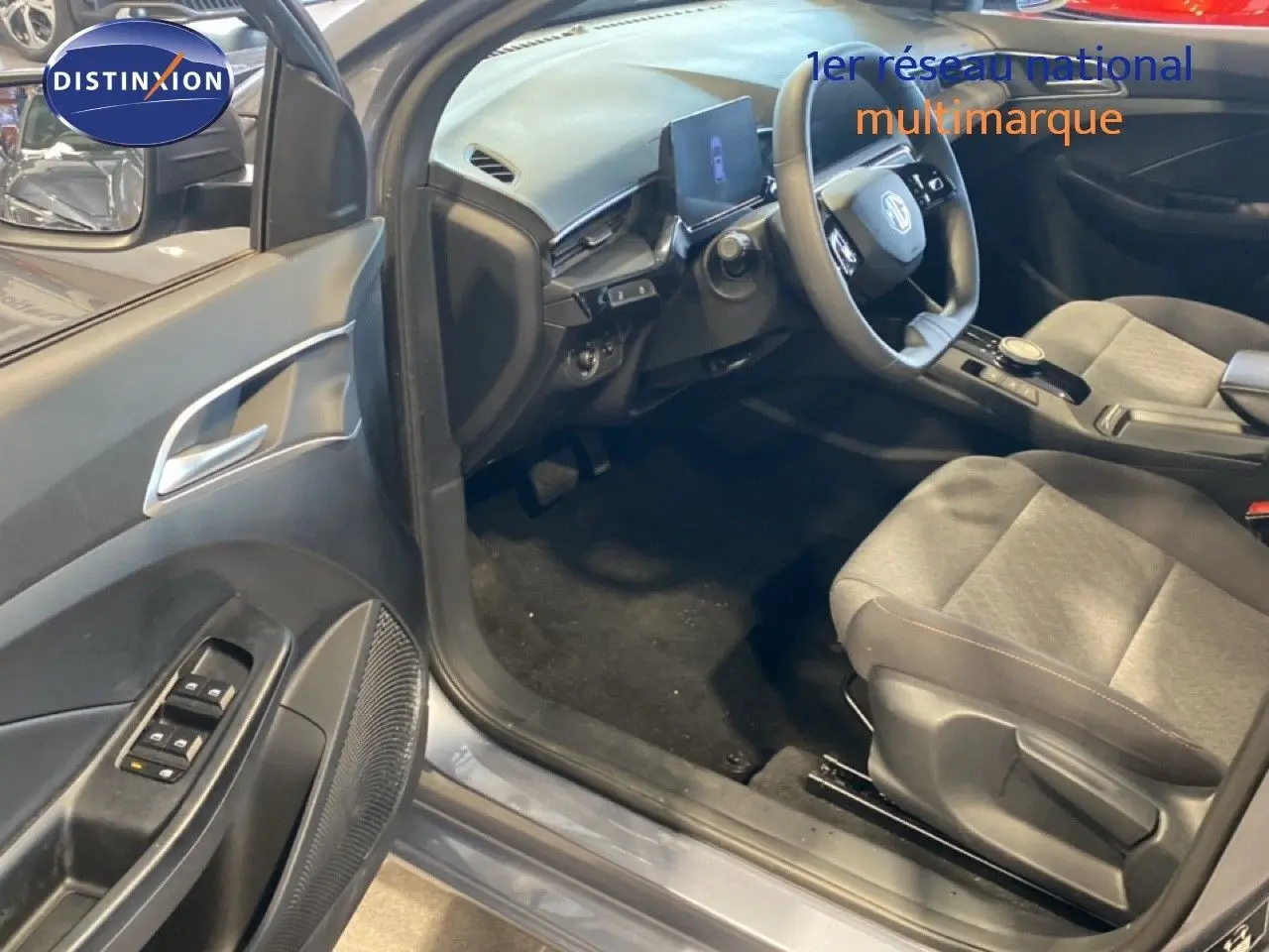 Vue intérieure côté conducteur de la MG3 1.5 Hybrid 2024 en gris Hampstead, montrant le tableau de bord et les sièges tissu gris.