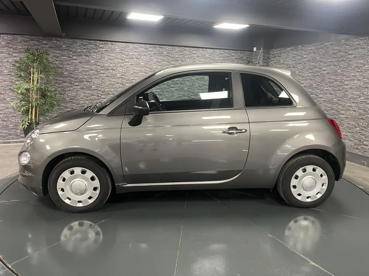 Profil droit d'une Fiat 500 gris métallisé 2023 avec jantes acier et rétroviseurs noirs dans un showroom.