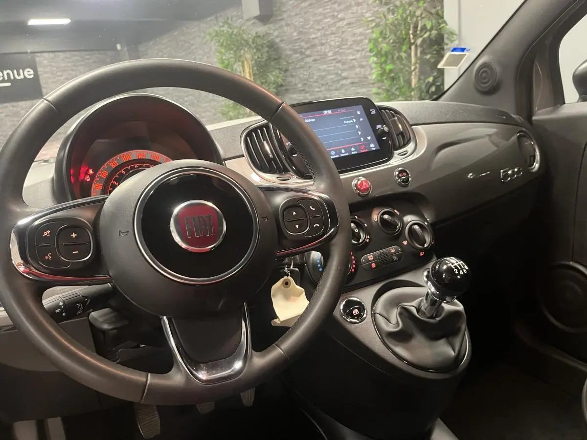 Intérieur noir de la Fiat 500 2023, vue du poste de conduite avec volant, tableau de bord et levier de vitesses manuel.