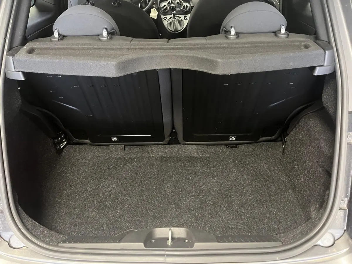 Coffre ouvert vu de l'arrière d'une Fiat 500 gris, montrant la banquette arrière rabattable et le tapis de coffre.
