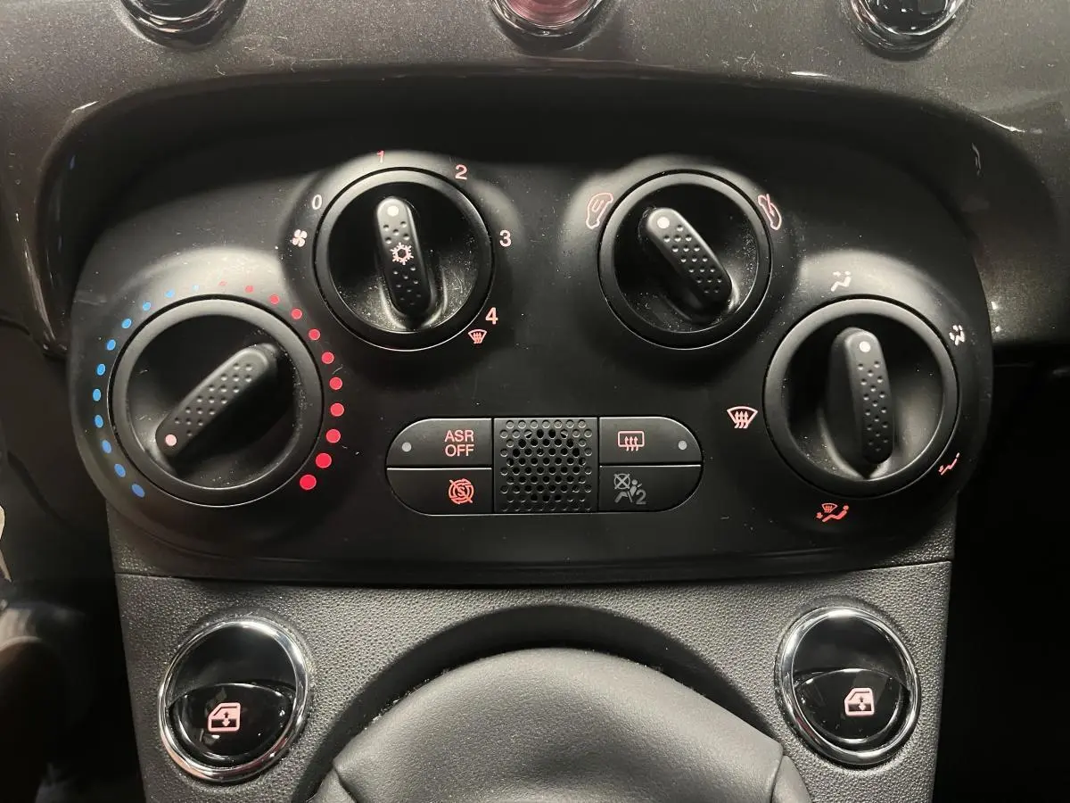 Gros plan sur les commandes de climatisation manuelle et vitres électriques de la Fiat 500 gris métallisé 2023.