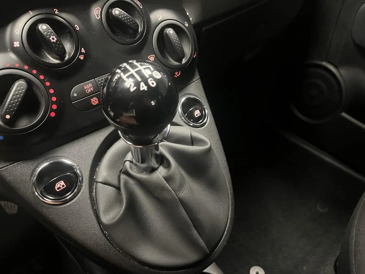 Le levier de vitesses manuel noir et les commandes de climatisation du tableau de bord d'une Fiat 500 gris 2023.
