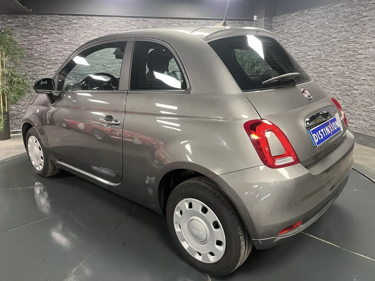 Fiat 500 gris métallisé vue 3/4 arrière droit, avec jantes acier et poignées de porte chromées.