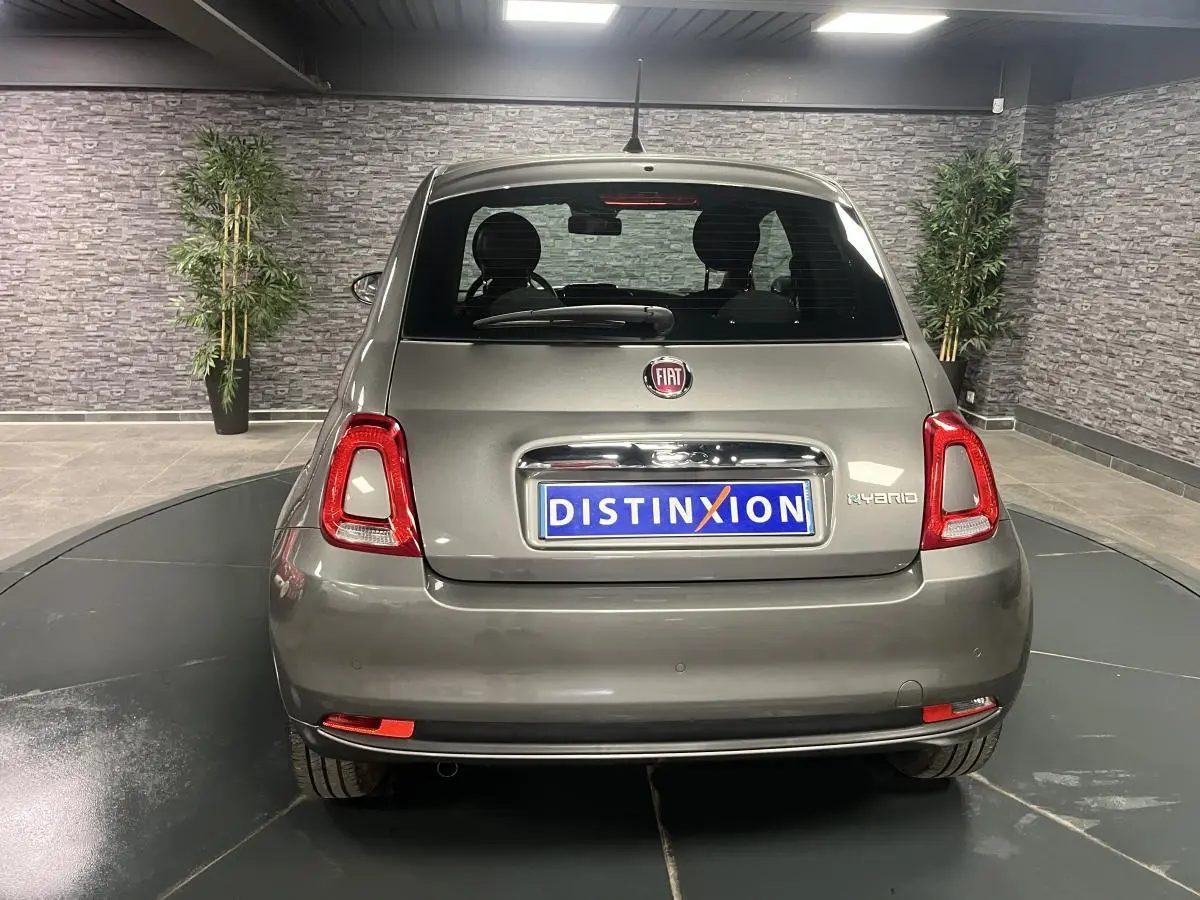 Vue arrière d'une Fiat 500 hybride gris métallisé avec logo Fiat et plaque Distinxion en intérieur showroom.