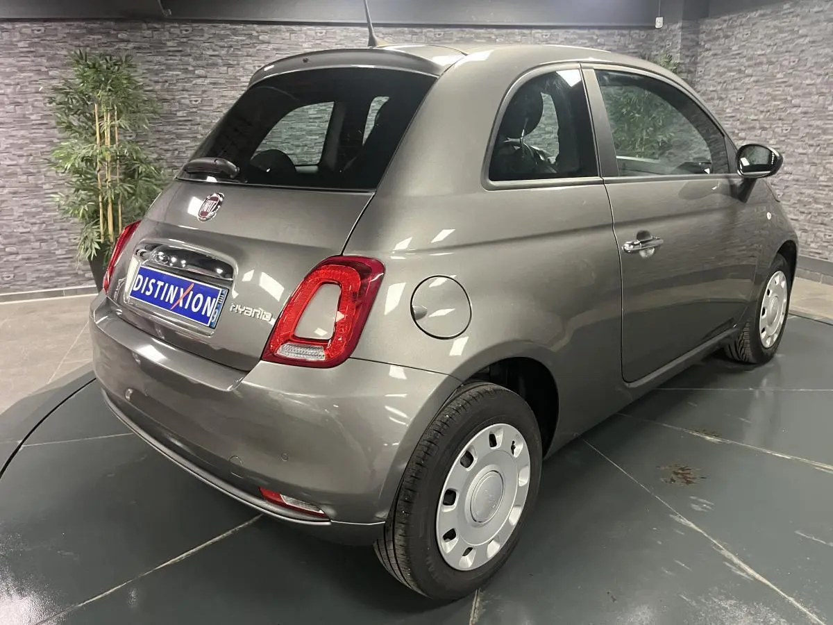 Vue 3/4 arrière droite d'une Fiat 500 hybride gris métallisé avec jantes acier et feux arrière LED dans un showroom.