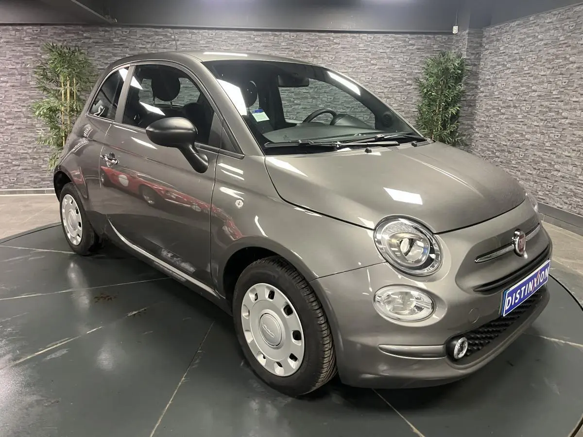 Fiat 500 gris métallisé vue 3/4 avant droit avec jantes acier et rétroviseurs noirs dans un showroom.