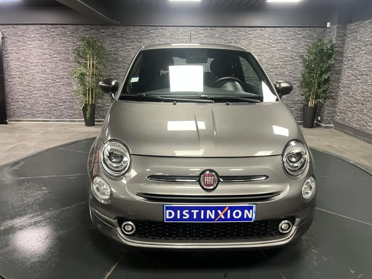 Vue avant d'une Fiat 500 gris métallisé avec projecteurs ronds et calandre chromée en intérieur showroom.