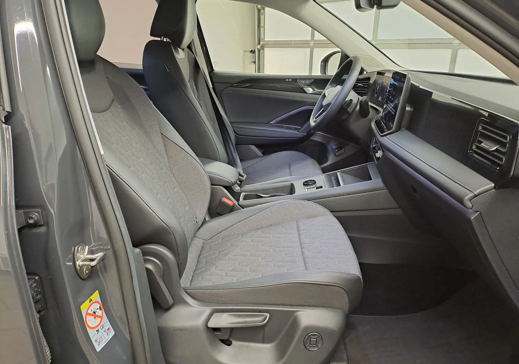Intérieur avant droit du Volkswagen Tiguan 2024 gris Urano, sièges tissu et tableau de bord moderne avec écran tactile.