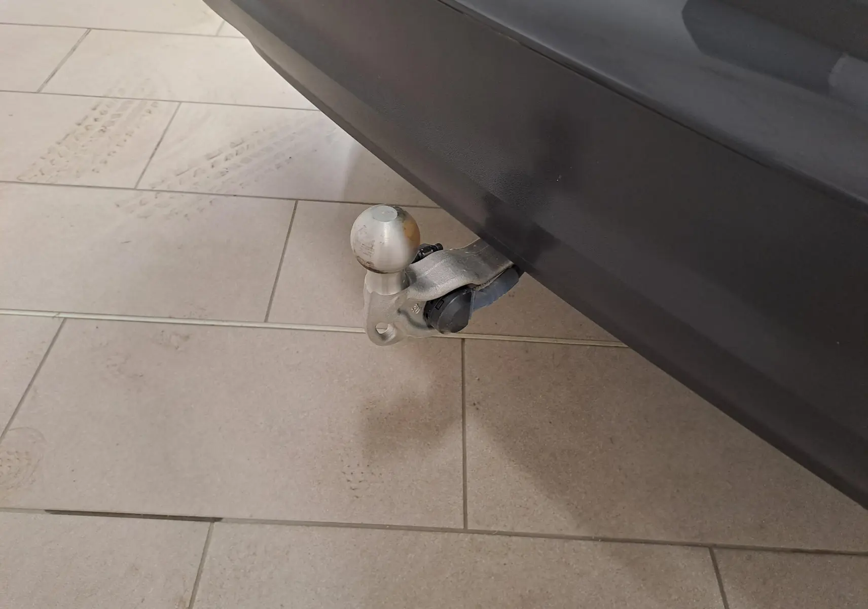 Gros plan sur le crochet d'attelage escamotable du Volkswagen Tiguan Gris Urano, visible sous le pare-chocs arrière côté droit.