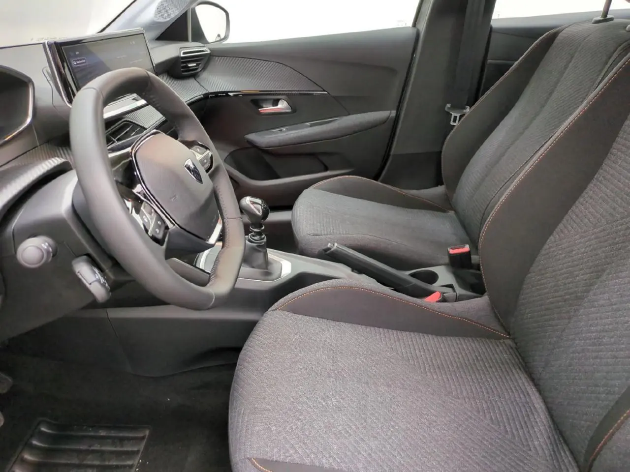 Intérieur avant droit de la Peugeot 208 gris clair, sièges tissu avec surpiqûres orange et volant compact cuir.