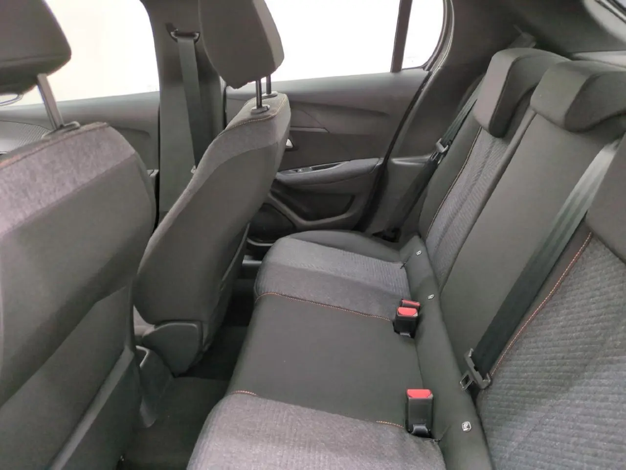 Vue intérieure arrière de la Peugeot 208 gris clair, sièges tissu avec surpiqûres orange Sunrise visibles.