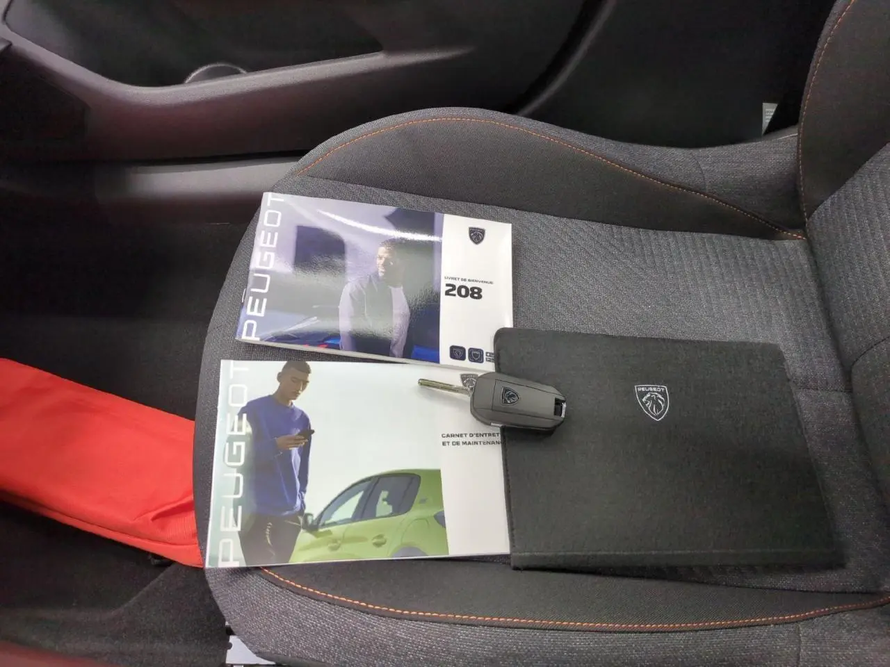Vue intérieure du siège avant droit gris clair d'une Peugeot 208 avec clés et manuels posés dessus.
