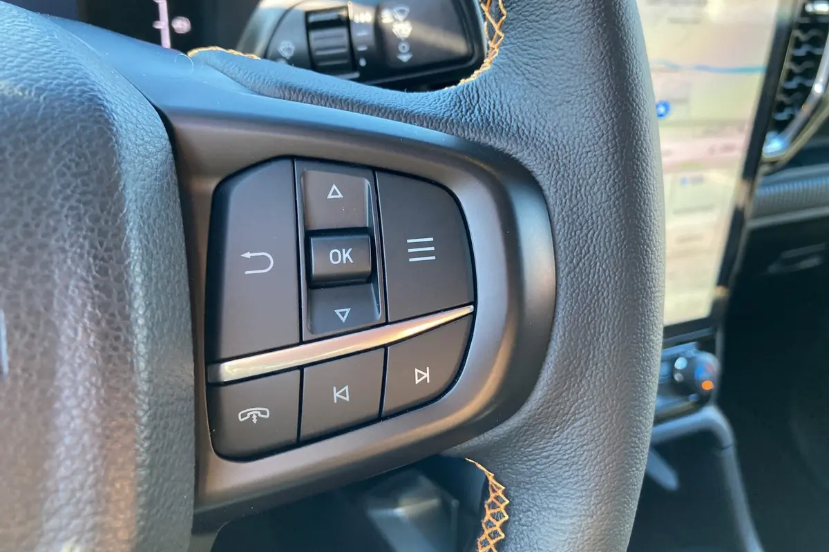 Gros plan sur les commandes multifonctions noires du volant cuir du Ford Ranger Wildtrak blanc glacier, avec surpiqûres orange visibles.