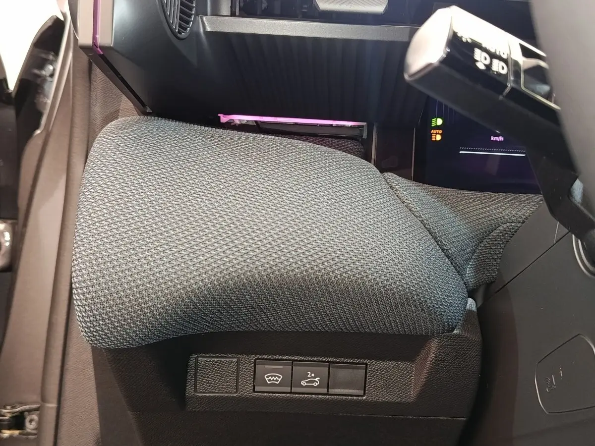 Gros plan sur l'accoudoir central gris et les commandes sous le volant du Citroën C5 hybride 2025.